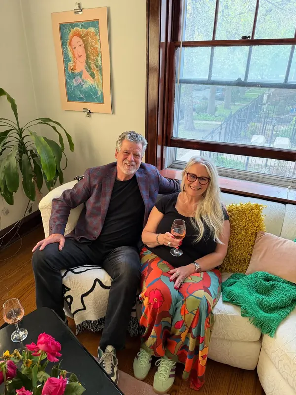 JanLee at home in a light-filled living room with colorful art, flowers and plants